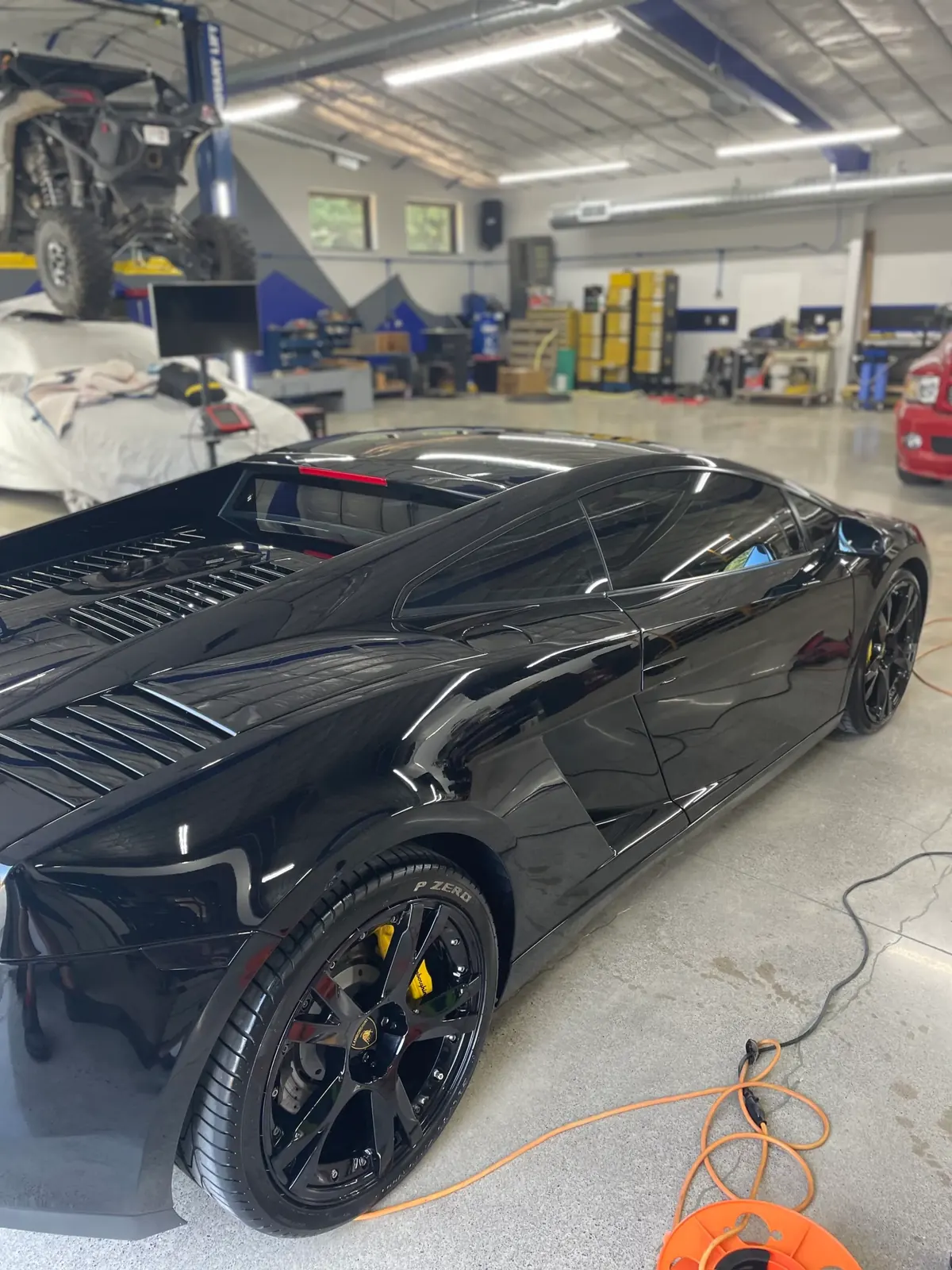 Polished black paint on a Lamborghini Gallardo's rear quarter panel, shop lights reflected in it