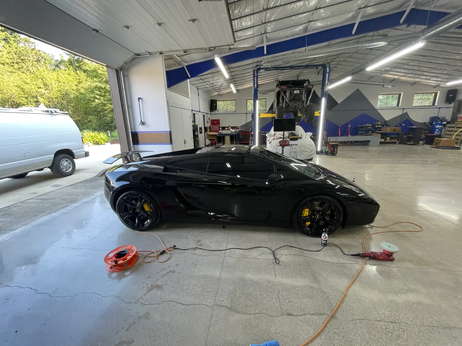 Black Lamborghini Gallardo mid-detail on Tan's shop floor, a dual-action polisher beside it