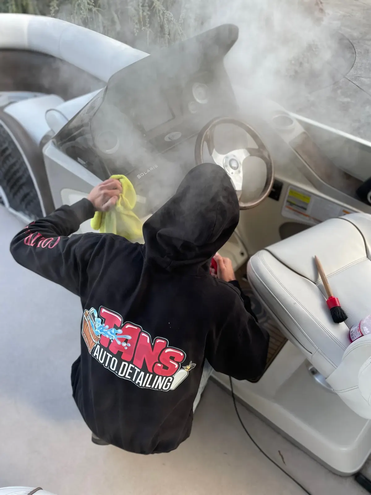 Tanner Coltrane in a Tan's Auto Detailing hoodie, steam-cleaning a boat dashboard